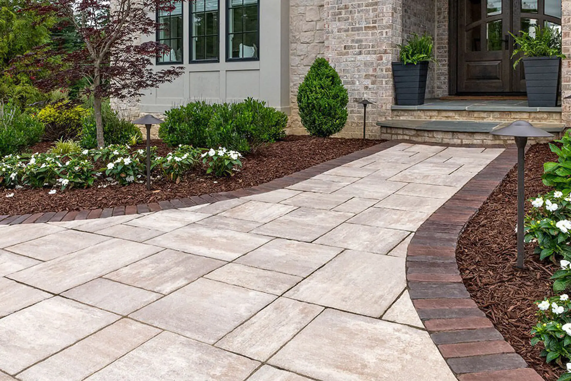 Wide front yard pathway with elegant concrete walkways leading to home entrance, bordered by brick edging.