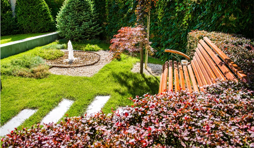 Beautiful backyard landscaping ideas with a fountain, lush greenery, vibrant plants, and a wooden bench.