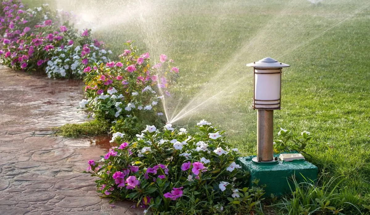 Sprinkler system watering flowers and lawn in a drought-resistant landscaping design with efficient irrigation.